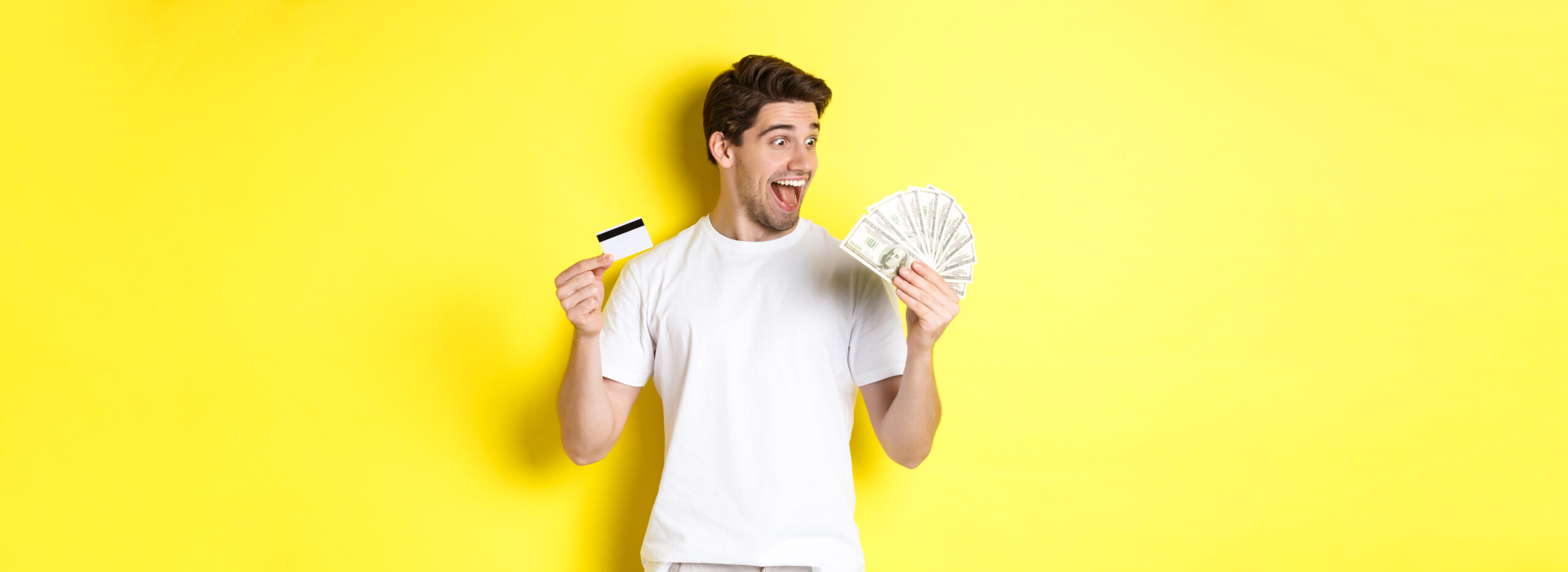 Rapaz, feliz, segurando várias notas de dinheiro em uma mão e cartão de crédito na outra