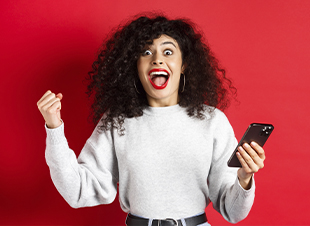Mulher jovem, com o celular na mão, comemorando por ter ganhado sorteio