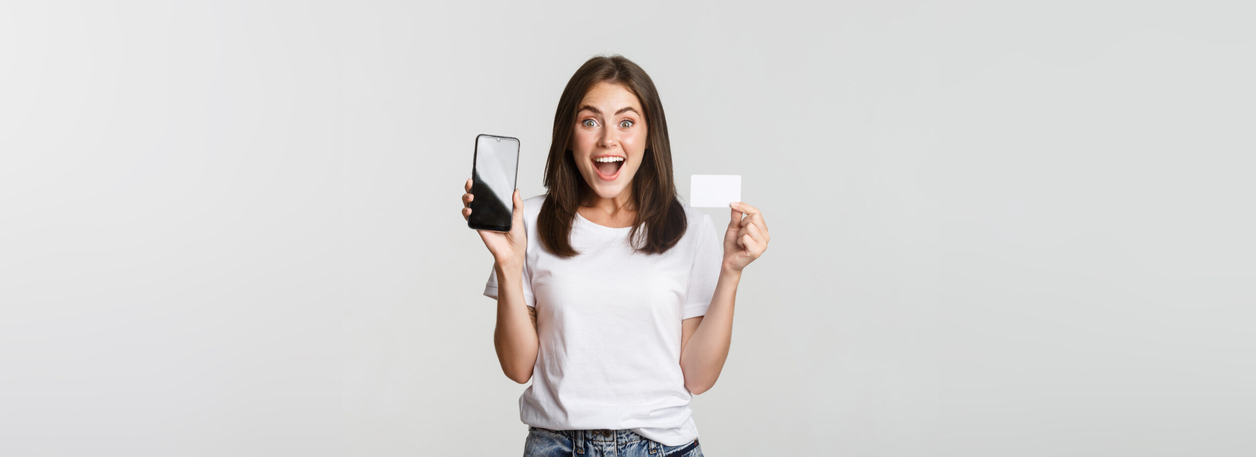 Excited and surprised cute girl showing credit card and mobile phone banking app on screen.