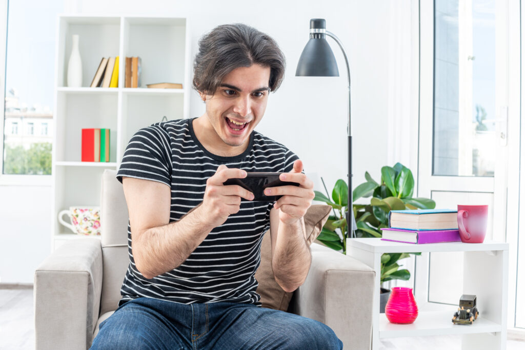 Homem jovem, sorrindo,jogando o jogo do aplicativo PostoAki no celular