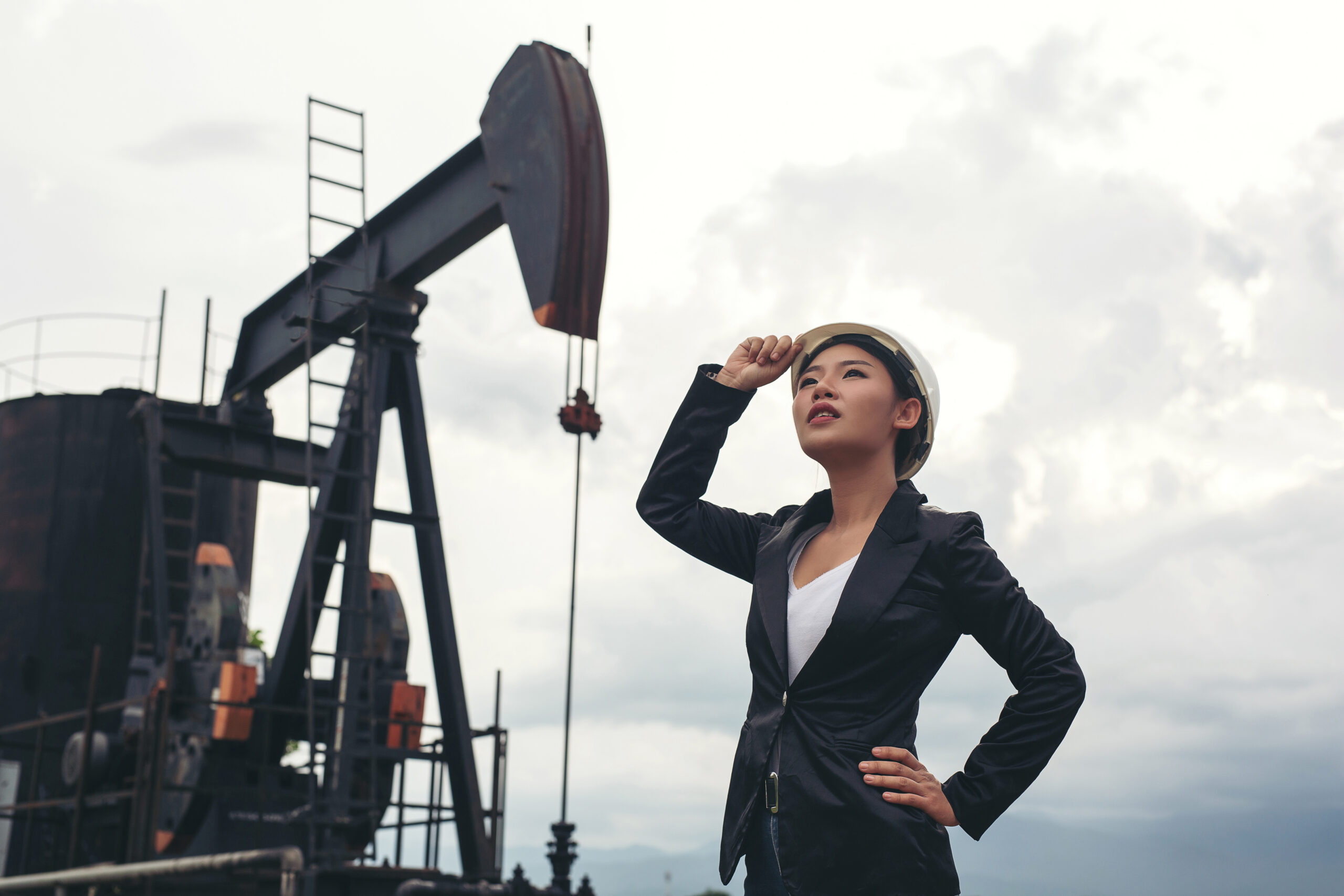 Female engineer standing with working oil pumps with a white sky background.
