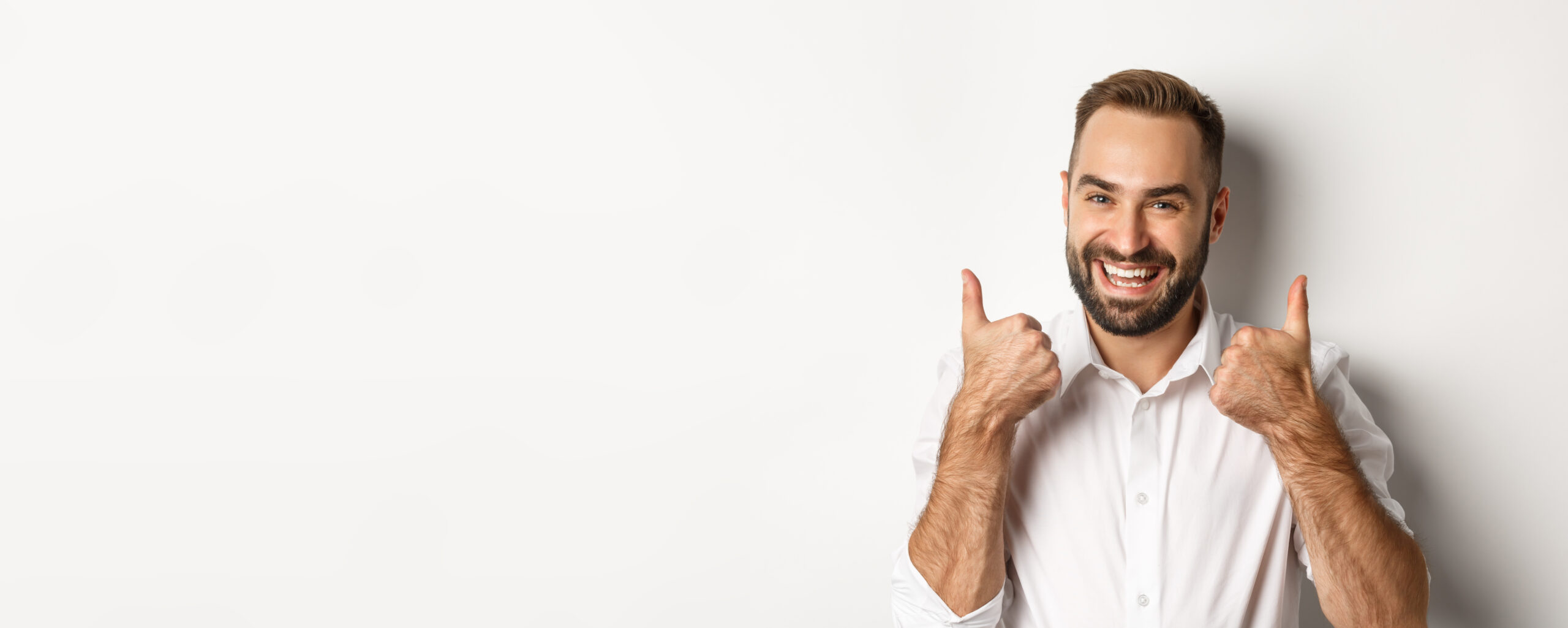 Close-up of satisfied bearded guy in white shirt, showing thumbs up in approval, like and agree, positive answer, white background.