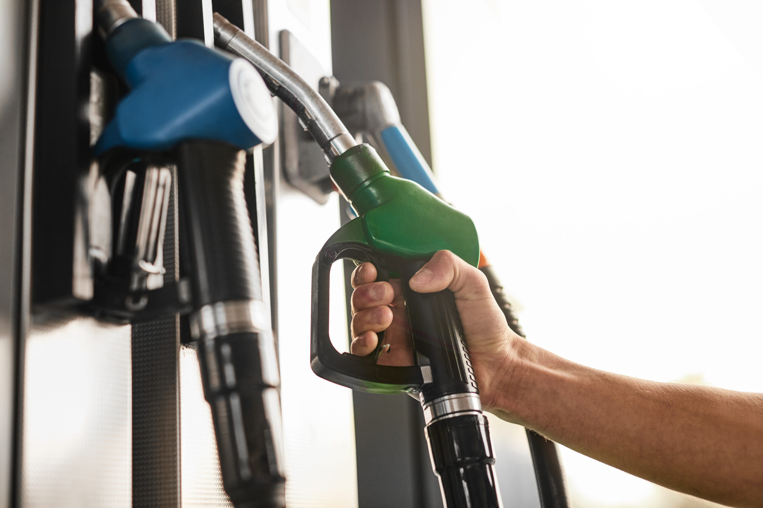 Low angle of anonymous male client taking pump nozzle from rack while visiting fuel station in city