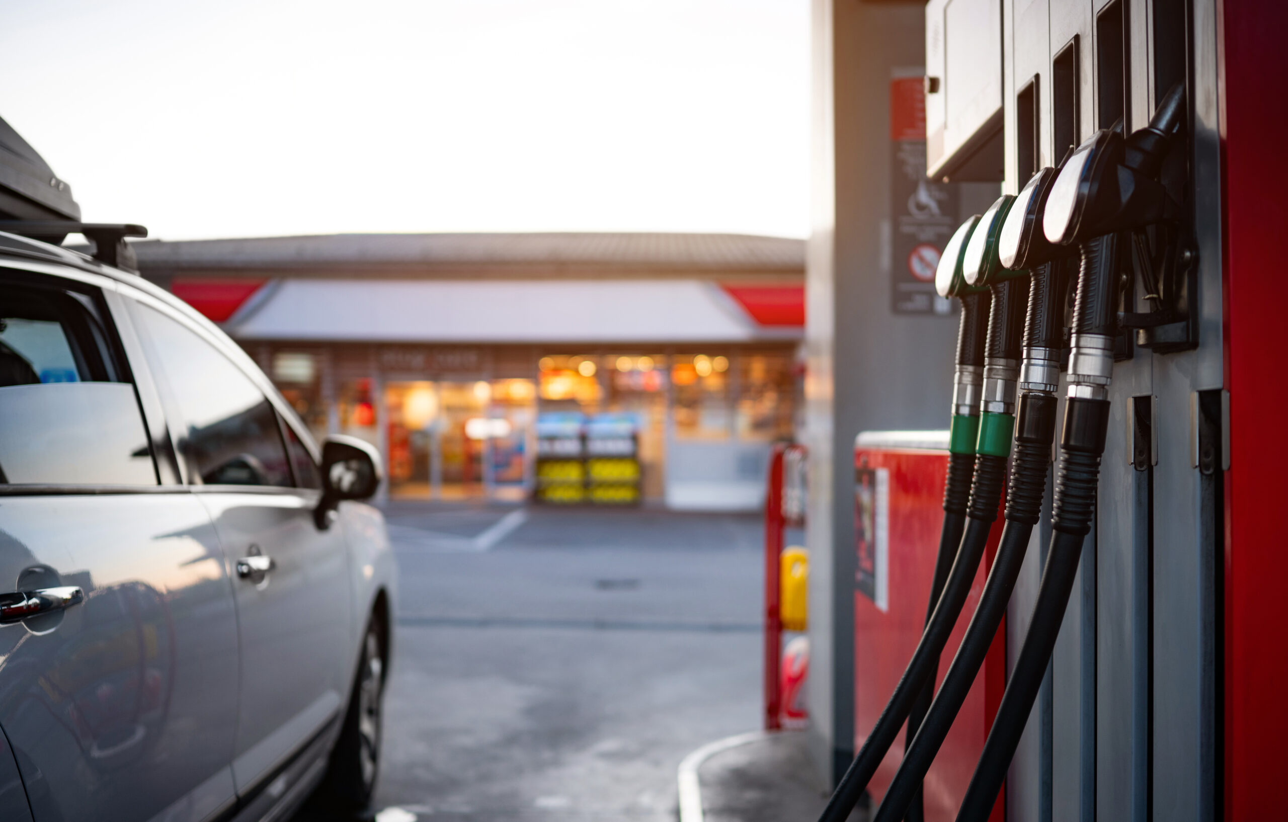 Car Parked At The Fuel Pump Of A Gasoline Station, With Petrol And Diesel Nozzles Hanging Nearby